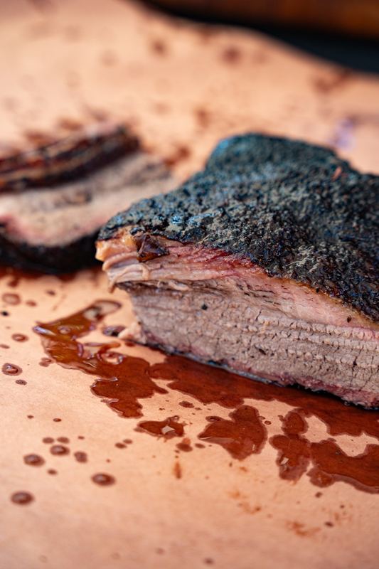 Sliced brisket with a heavy black bark resting on butcher paper in its own juices