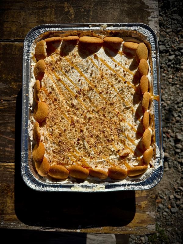 Banana pudding in a full pan, ringed with vanilla wafers and drizzled with caramel