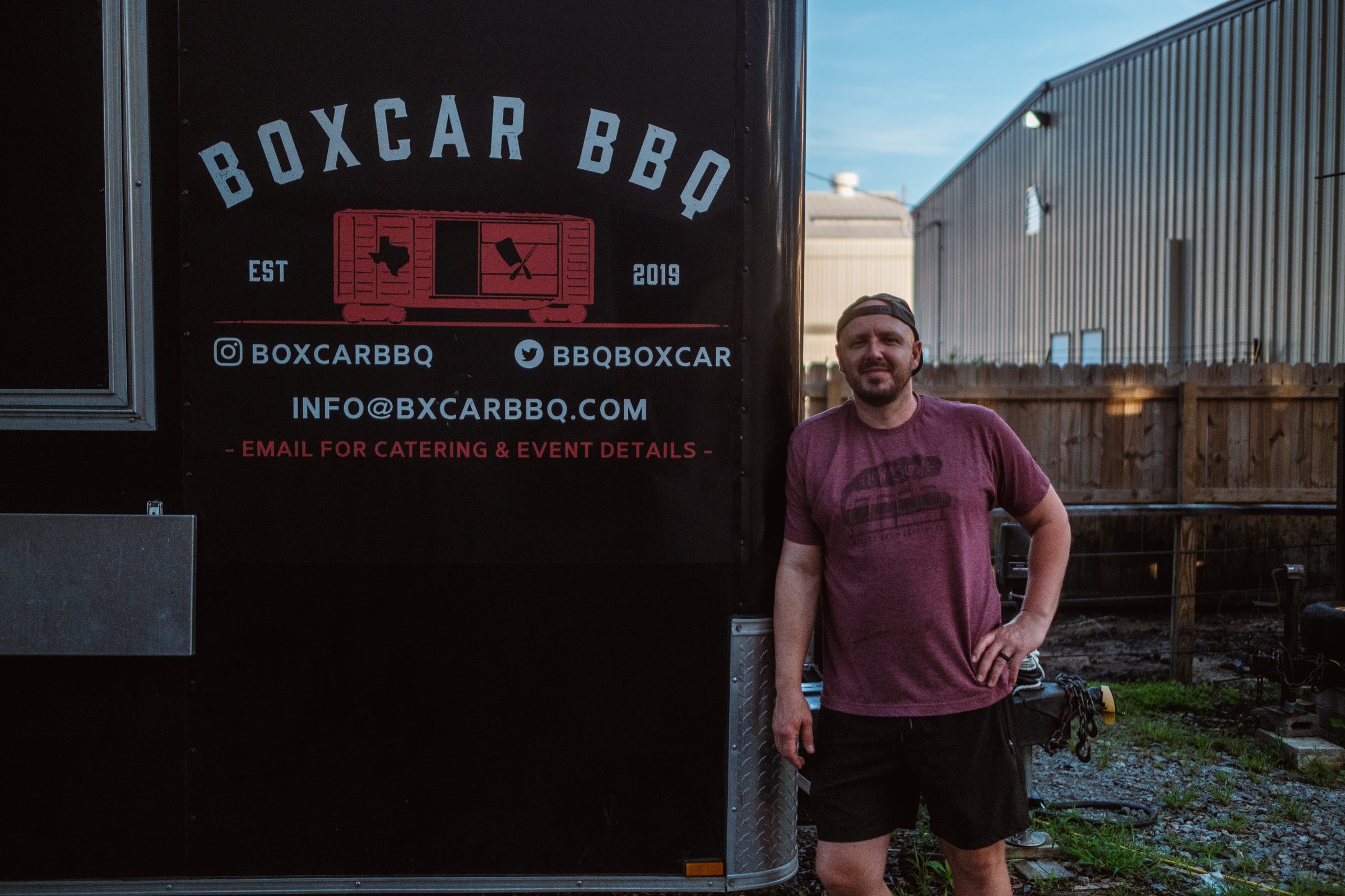 Jeremy smiling beside the Boxcar BBQ trailer sign