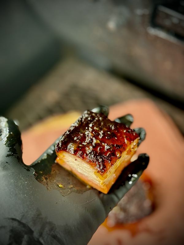 Glazed pork belly bite on a gloved hand